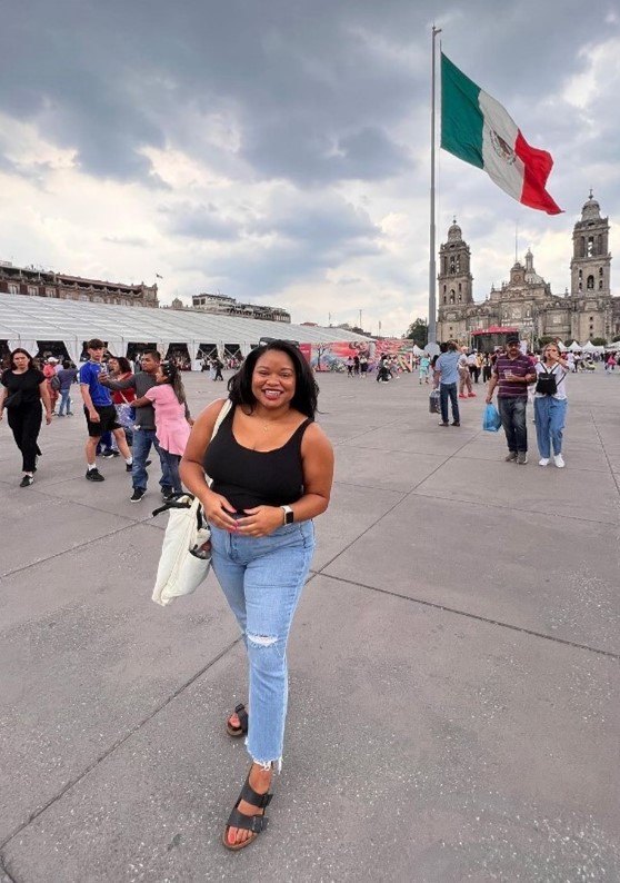 Ashley standing in a plaza with a Mexican flag behind her.