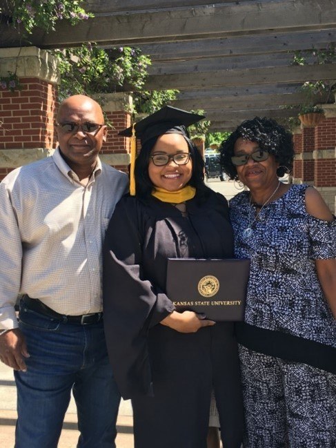 Ashley in a graduation cap and gown holding a diploma, standing in between her parents.