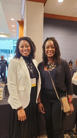 Two women posing together and smiling in a conference hallway.