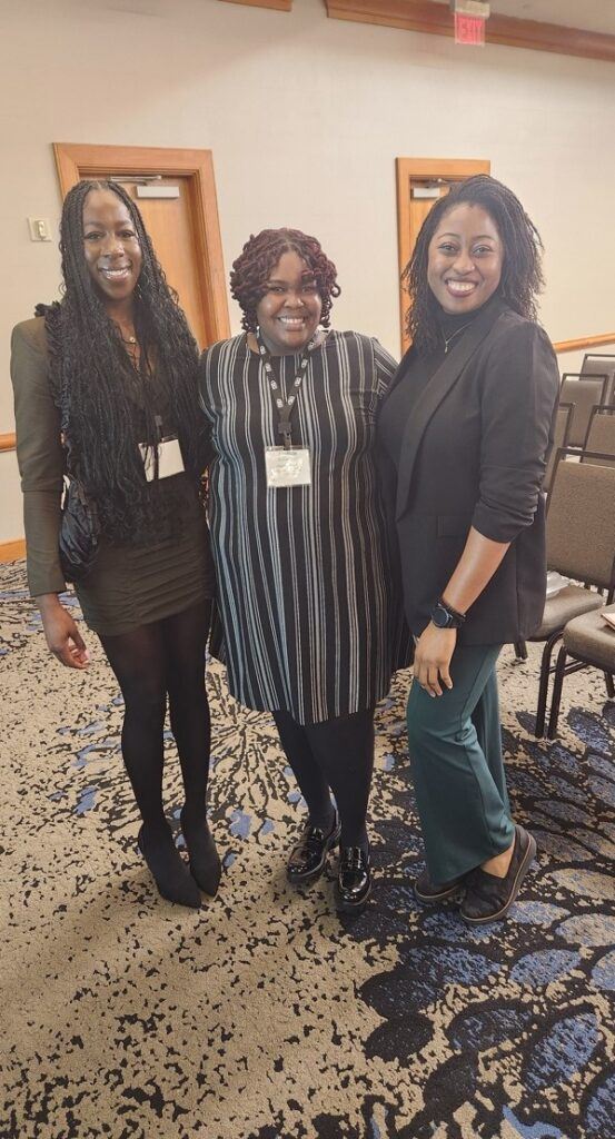 A group of three women posing and smiling together in a conference hallway.