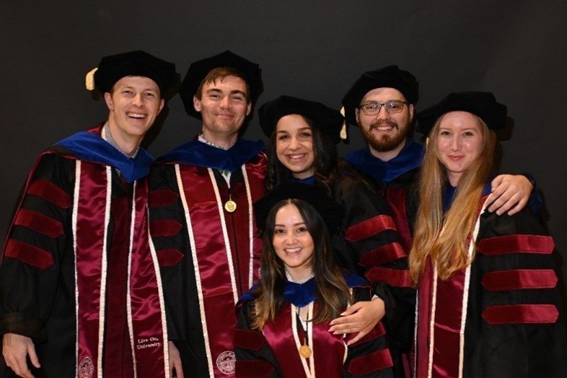 Sam posing with a group of her friends in cap and gown.