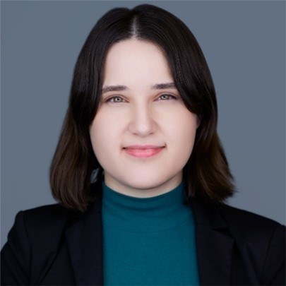 A person with dark hair wearing a suit and green turtleneck.