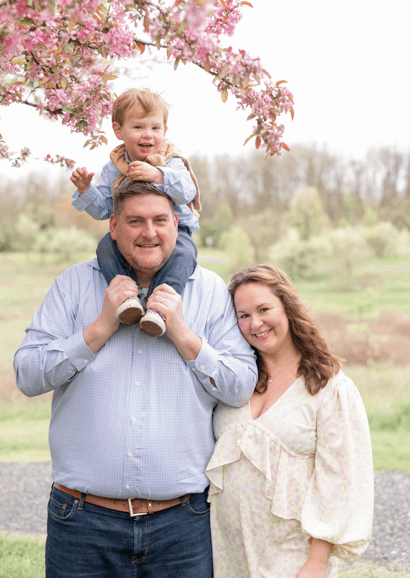 A woman and man posing with a child on the man's shoulders.