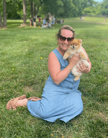 A woman holding a small dog while sitting on grass.