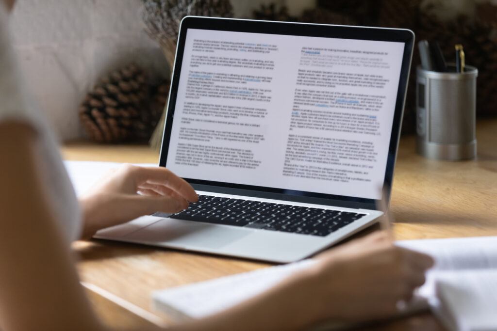 Close up view of modern technology digital gadget opened computer with electronic documents on screen. Young woman preparing report or reading scientific article, studying at home, education concept.