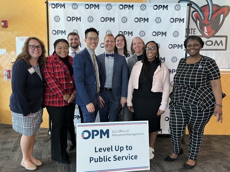 A group of people standing behind a sign that reads "OPM Level Up to Public Service."