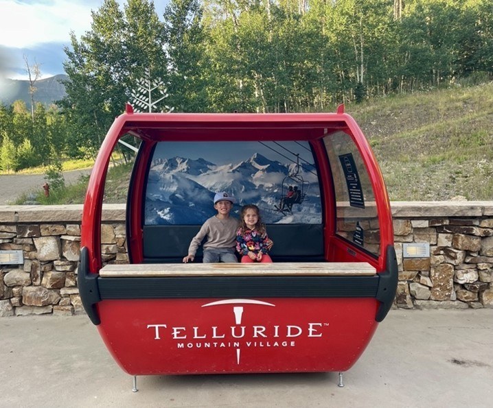 Ashley's children sitting and smiling in a display gondola at Telluride Mountain Village.