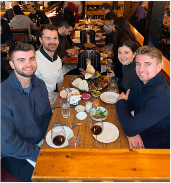 A group of people sitting at a restaurant table with wine glasses and various plates of food.